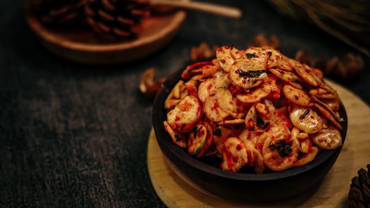hero-img-02 Close-up of a spicy fried snack served in a rustic wooden bowl on a dark background.