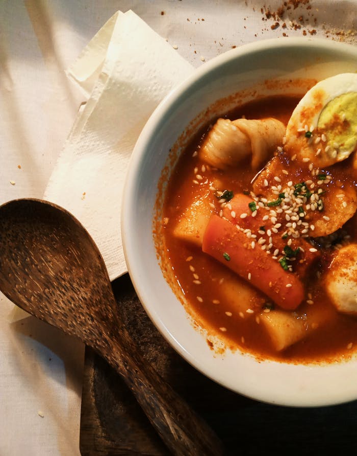 services-03 A mouthwatering bowl of spicy Korean Tteokbokki garnished with sesame seeds and herbs.