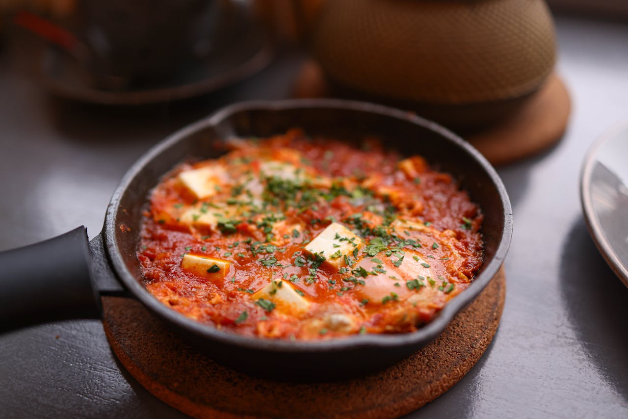 why-choose-us Appetizing shakshuka in a skillet, topped with cheese and fresh herbs, perfect for a hearty breakfast.